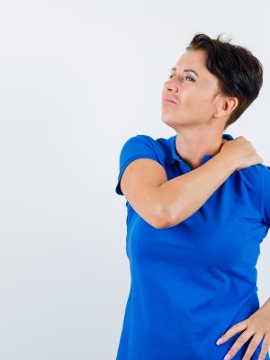 mature woman suffering from shoulder pain in blue t-shirt and looking tired. front view.